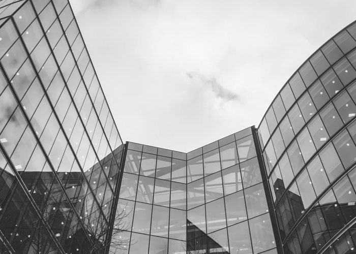 Bâtiment moderne en verre sur fond de ciel nuageux.