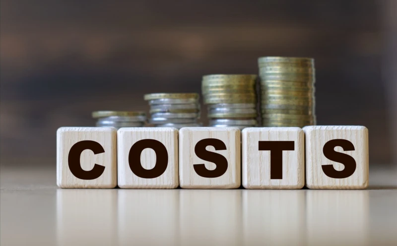 Wooden blocks spelling costs with stacked coins behind.